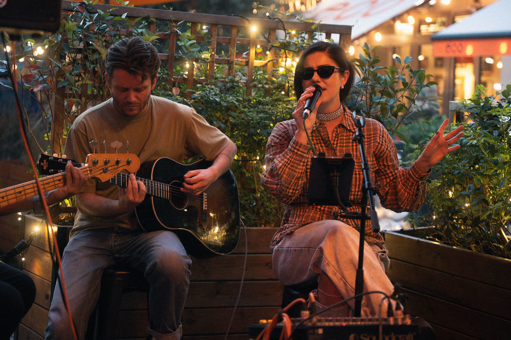 Two musicians performing outside, one is singing and the other is playing acoustic guitar.