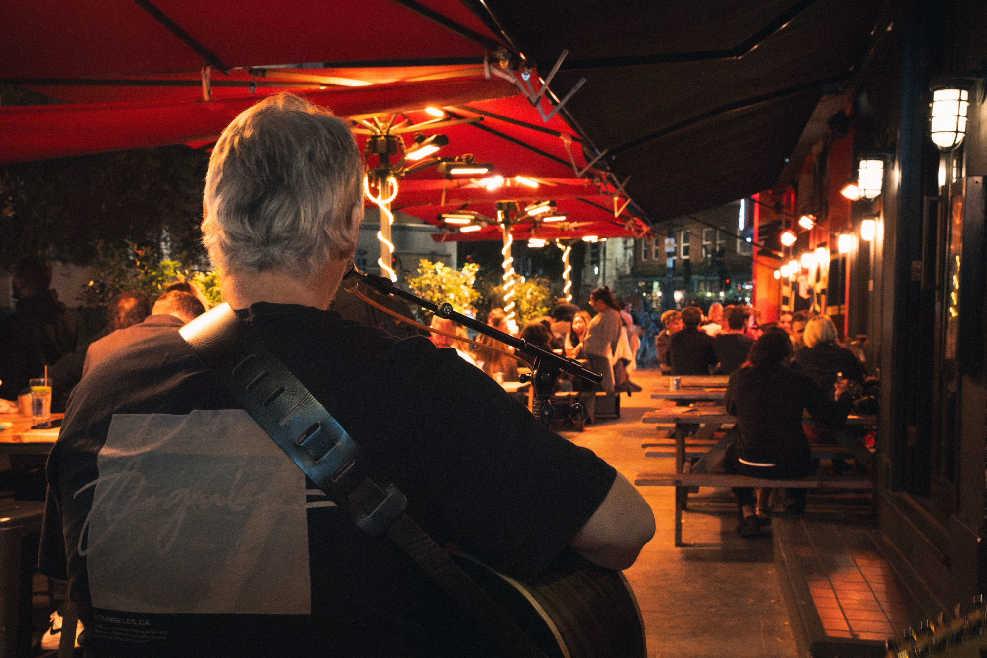 A man playing acoustic guitar in a beer garden in the evening.