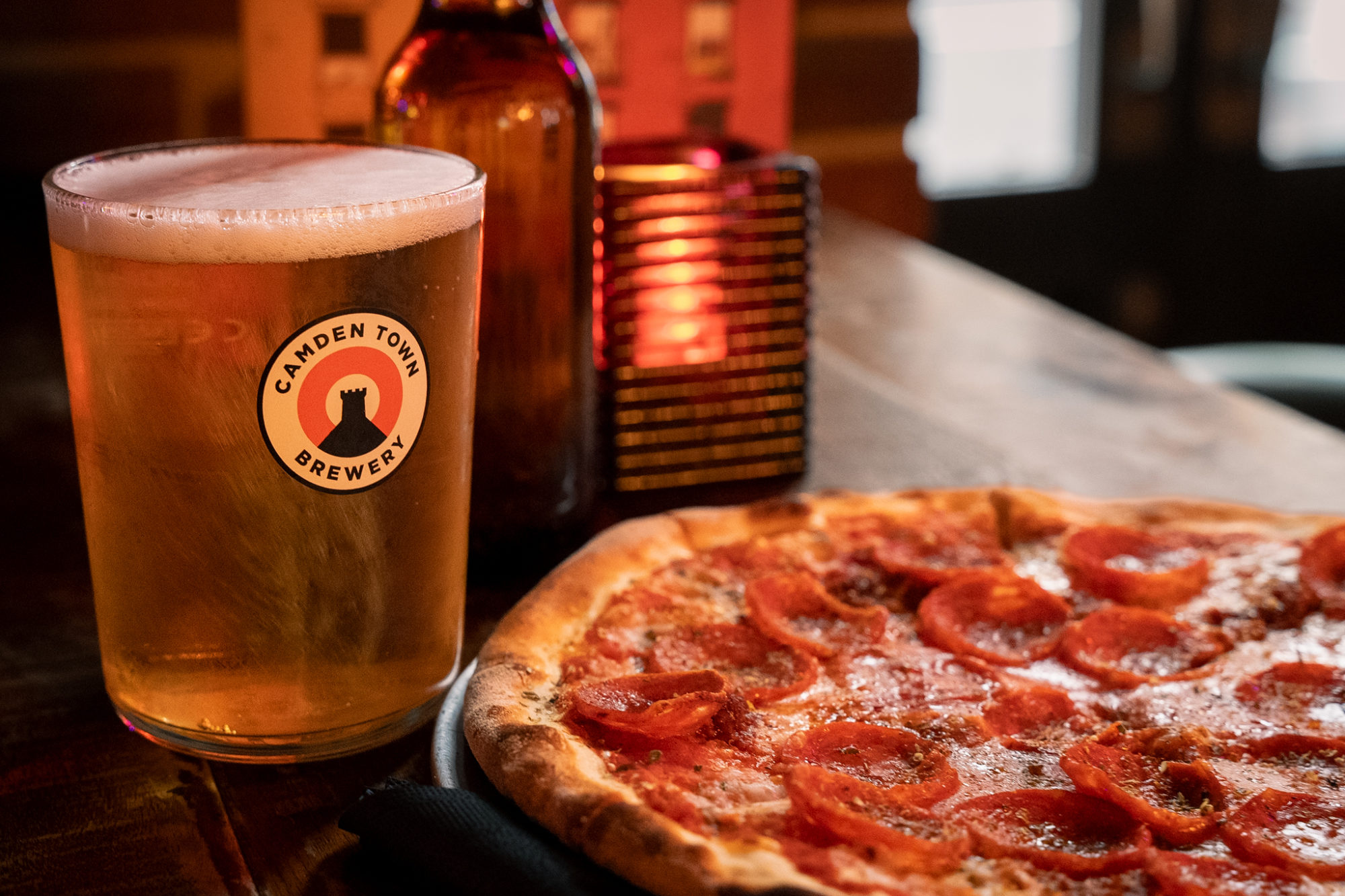 A pint of cold beer next to a pepperoni pizza.