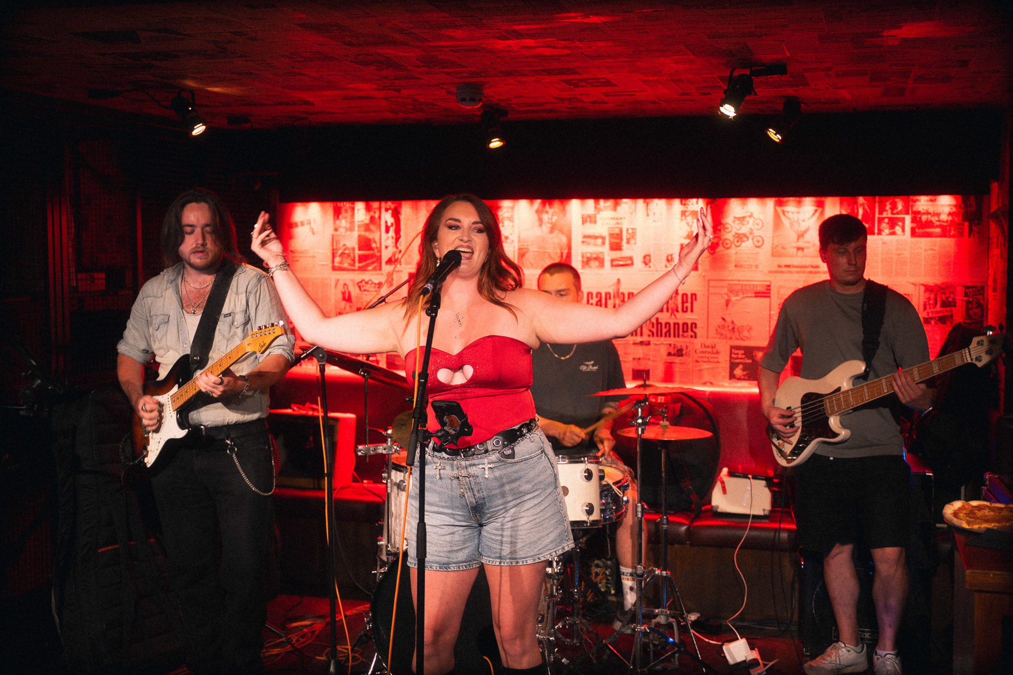 A band playing musical instruments such as drums and electric guitar with a female lead singer.