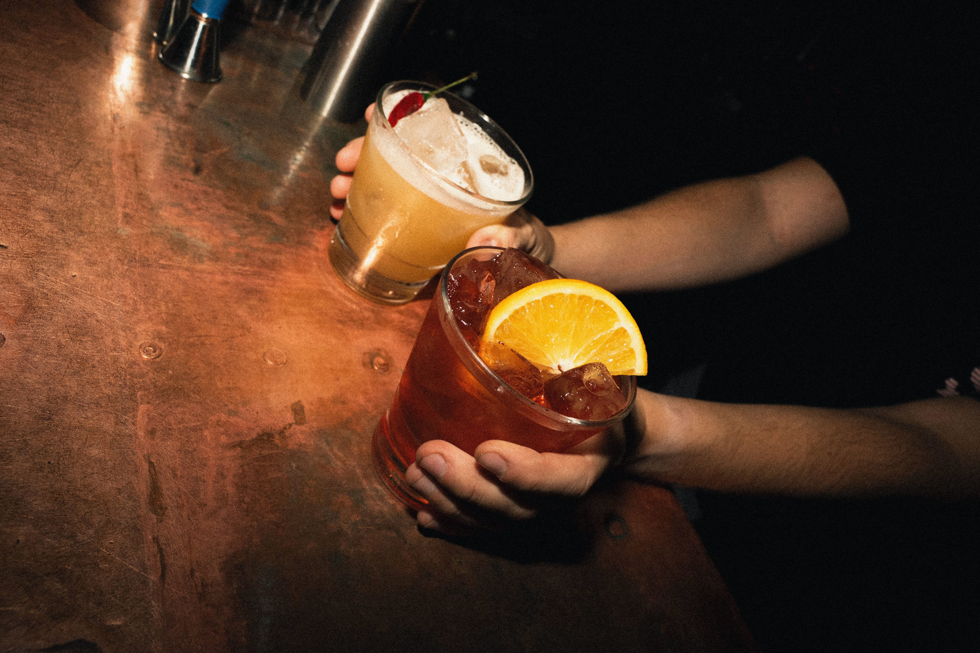 A margarita cocktail with a red chilli pepper and a negroni with a slice of orange in it.