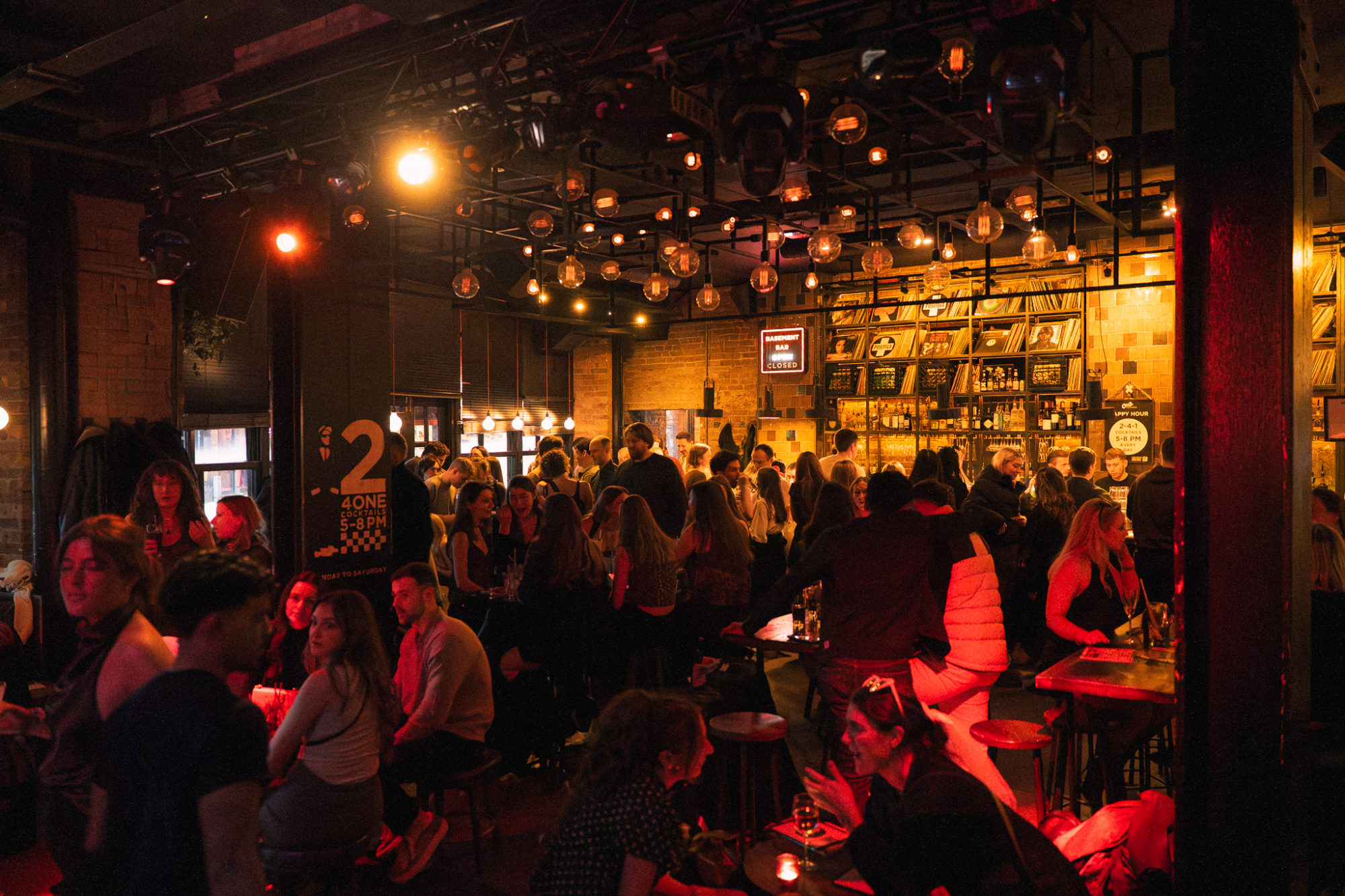 People standing and sitting in a live music venue that has vinyl records on the wall.