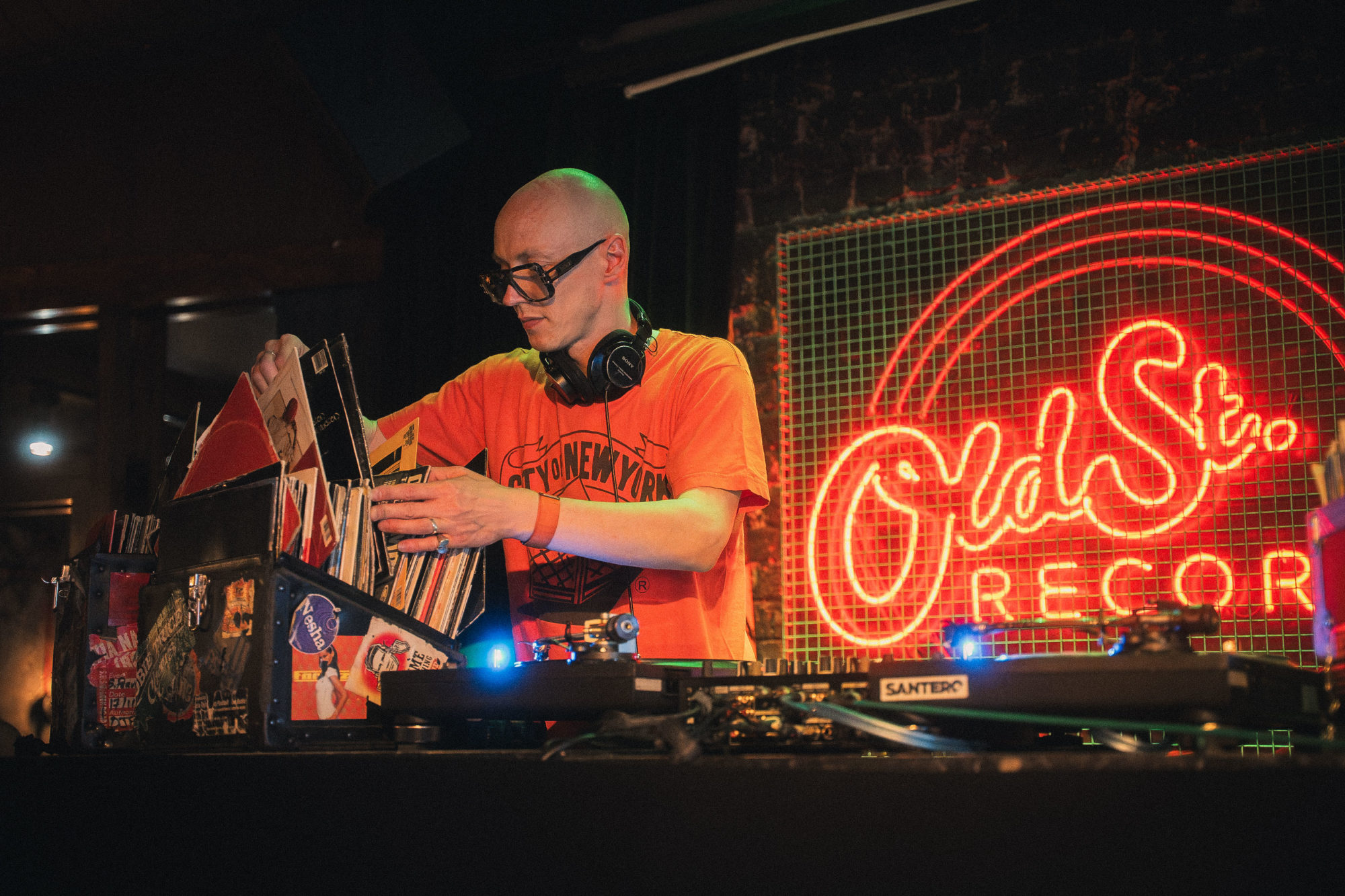 A DJ in an orange t-shirt holding records.